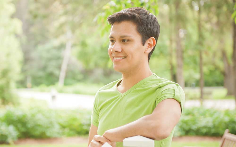 joven de cabello castaño sentado y sonriendo al aire libre