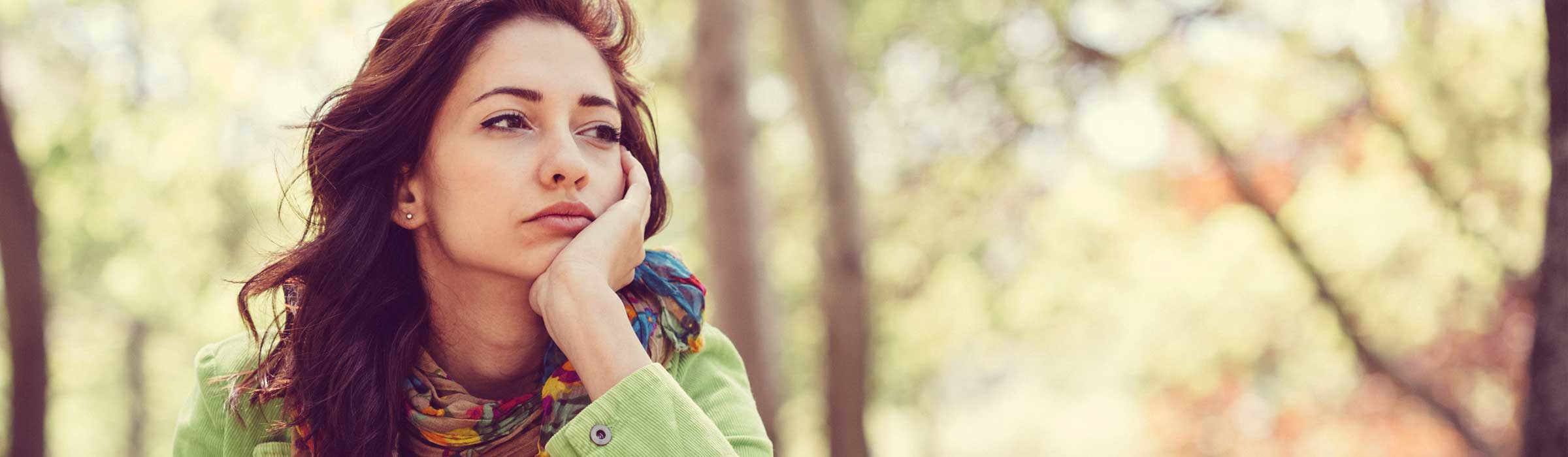 woman in green coat staring sadly by trees