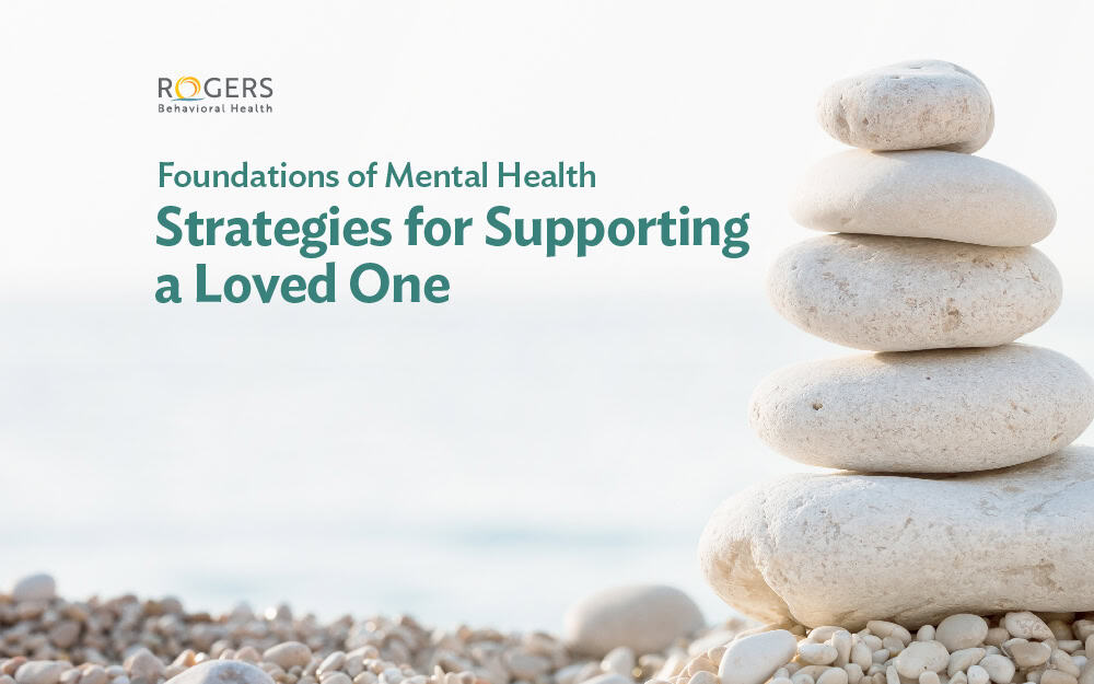 The image features a stack of smooth, rounded stones on the right side, balanced on top of each other against a soft, blurred background with a gradient fade from white to light blue. The stones are beige with subtle textures, varying slightly in size, and appear to be carefully arranged. On the left side, text says "Strategies for supporting a loved one."