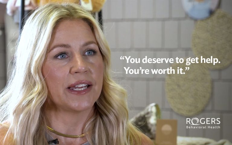 The image features a woman with long, wavy blonde hair and blue eyes, looking slightly off-camera. She appears to be speaking. The background is softly blurred, showing circular decorative objects and other indistinct elements. In the foreground, white text is displayed on the right side of the image, containing a motivational statement. In the lower right corner, "You deserve to get help. You’re worth it.”