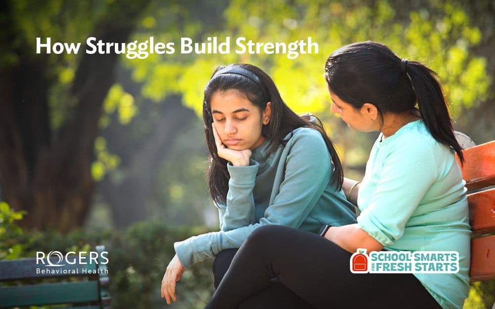 The image shows two individuals sitting on a wooden bench outdoors, surrounded by lush greenery. One person, a young woman wearing a light blue long-sleeve top, sits with her head on her hand, looking downcast. Beside her, another person in a teal shirt appears to be offering comfort and support. The background is out of focus, highlighting the trees and foliage, which provide a calming natural setting. The sunlight filters through the leaves, creating a warm ambiance. Transcribed Text: "How Struggles Build Strength