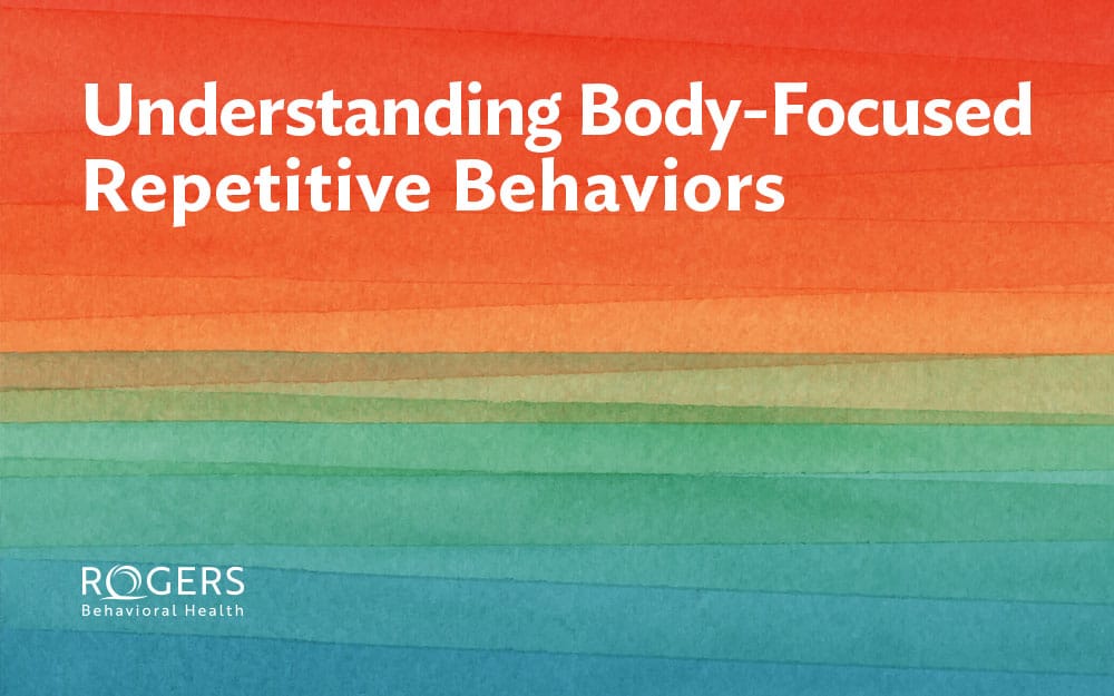 The image features a gradient background composed of horizontal watercolor stripes, transitioning from red at the top through orange, green, and blue toward the bottom. The text "Understanding Body-Focused Repetitive Behaviors" is prominently displayed in white, bold letters towards the top.