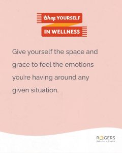 The image features a soft pink background with a prominent red ribbon at the top containing white text. The ribbon has two segments, with the top part reading "Wrap Yourself" and the lower part reading "In Wellness," each segment separated by a small orange triangle. Below the ribbon is a motivational message in dark gray text: Give yourself the space and grace to feel the emotions you’re having around any given situation.