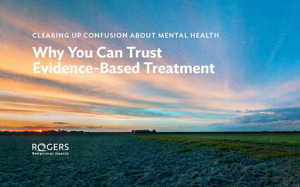 The image features a scenic landscape with an expansive sky displaying a gradient of colors from orange and pink near the horizon to blue higher up. The foreground consists of a vast field with neatly plowed soil extending towards a distant horizon, creating a sense of openness and tranquility. The image includes text overlayed on the sky. Text reads: "CLEARING UP CONFUSION ABOUT MENTAL HEALTH Why You Can Trust Evidence-Based Treatment