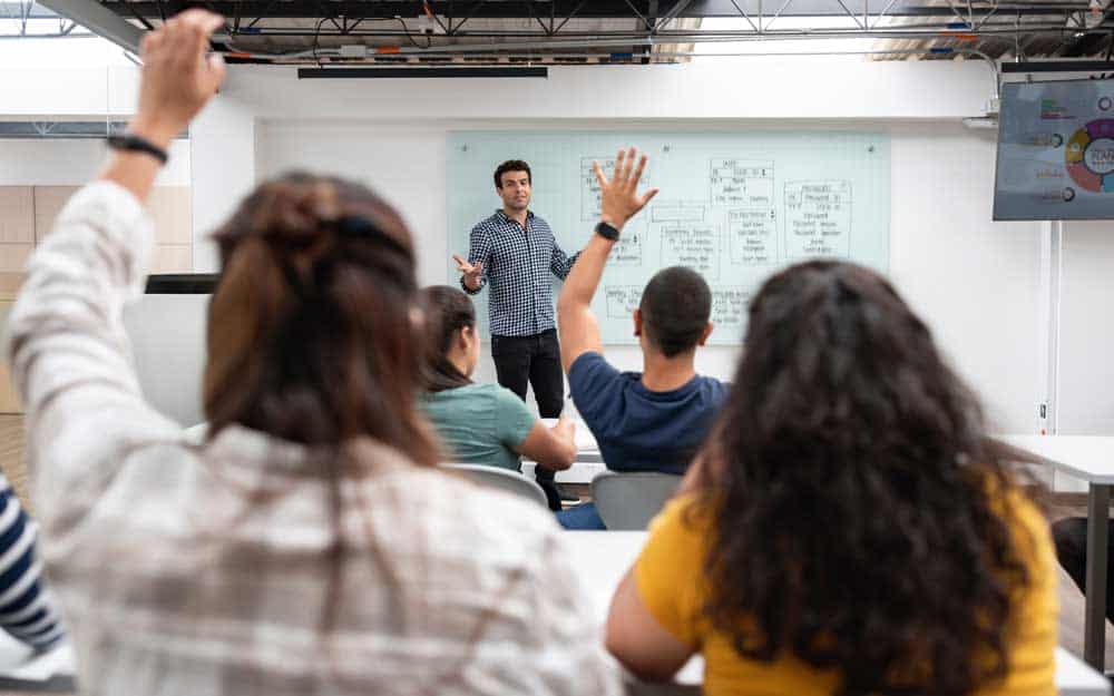 Teacher in a classroom with students raising hands