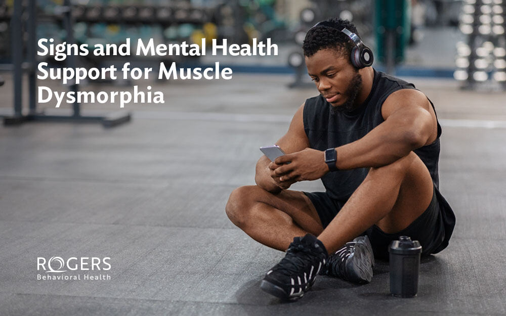 The image shows a man sitting on the floor of a gym after just working out to address anxiety about his muscles