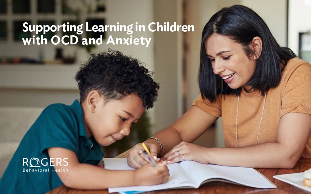 The image features a young boy doing his homework. His mom is heling since he has OCD. Text says: "Supporting Learning in Children with OCD and Anxiety."