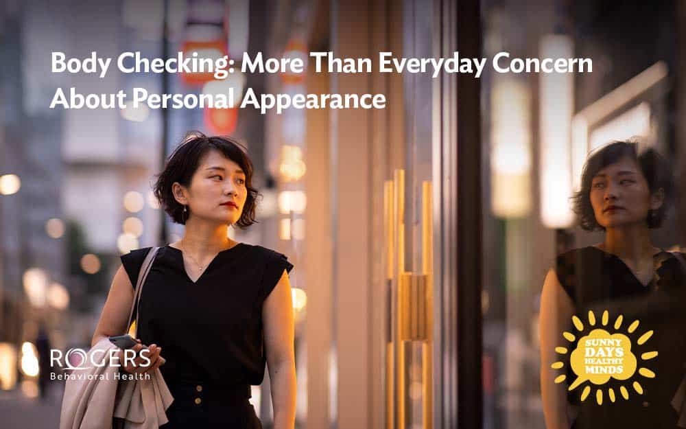 Image shows an Asian woman stopping by a store front to look at her reflection in the window as part of her body checking behaviors.