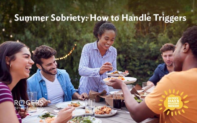 The image depicts a diverse group of people seated around a picnic table outdoors. They're talking and laughing, enjoying a summer meal without substances.