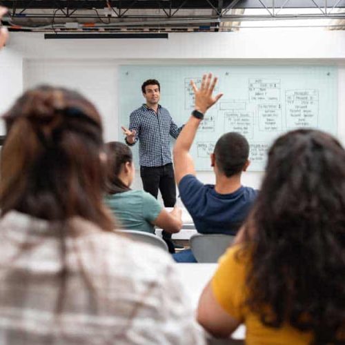 Teacher in a classroom with students raising hands